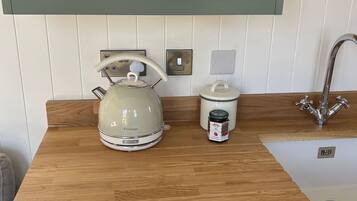 Een keuken met een waterkoker, een potje jam en een magnetron boven de aanrecht.