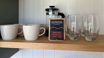 A shelf with coffee maker, mugs, and glasses.