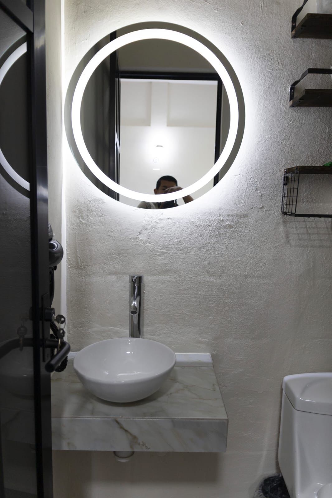 Ett badrum med ett vitt handfat, en spegel med en rund lampa och en toalett.