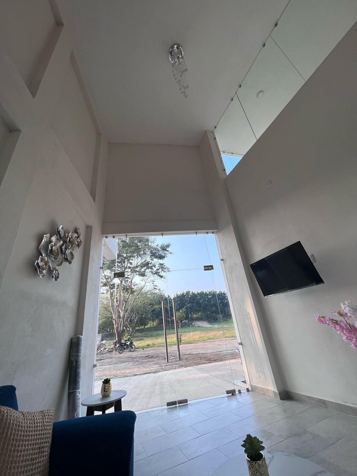 Una habitación amplia con un gran ventanal, un televisor de pantalla plana montado en la pared y un sofá azul.