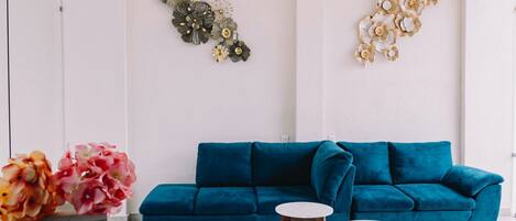 A modern living room with a teal sofa, two white round tables, and decorative wall art.