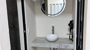 Un baño con un lavabo blanco, un espejo redondo, un perchero para toallas y un secador de pelo.