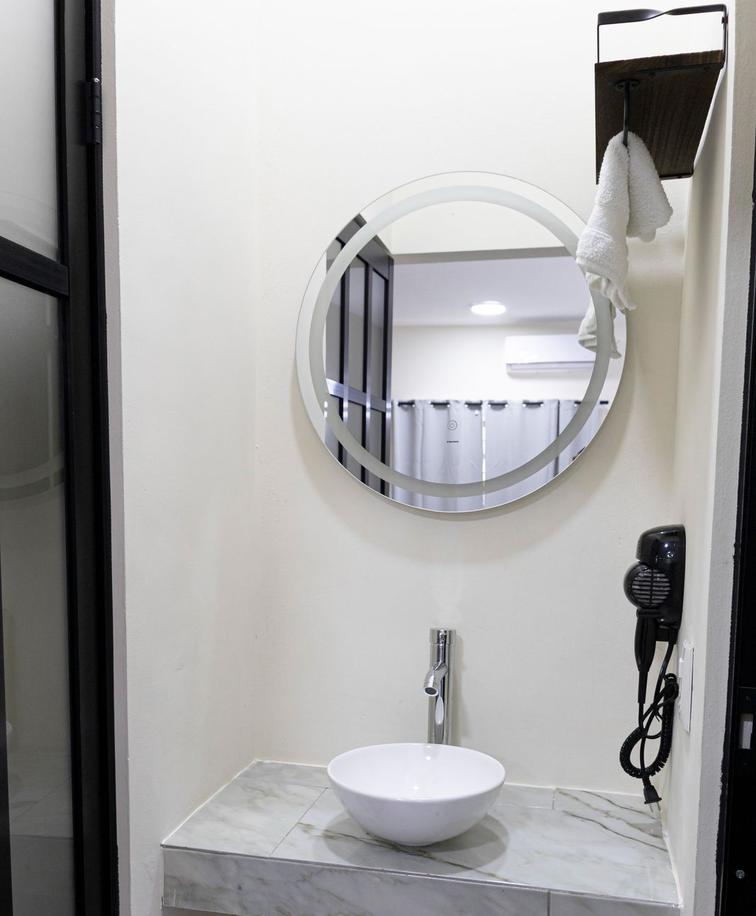 A bathroom with a round mirror, a white sink, and a hairdryer on the wall.
