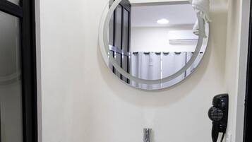 A bathroom with a round mirror, a white sink, and a hairdryer on the wall.