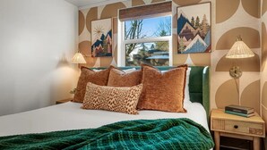 A bedroom with a bed, green blanket, and pillows, a window with a view, and two wall-mounted lamps. - The Happy Hideaway (Seattle)