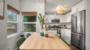 A modern kitchen with white cabinets, stainless steel appliances, and a wooden dining table with green chairs. - The Happy Hideaway (Seattle)