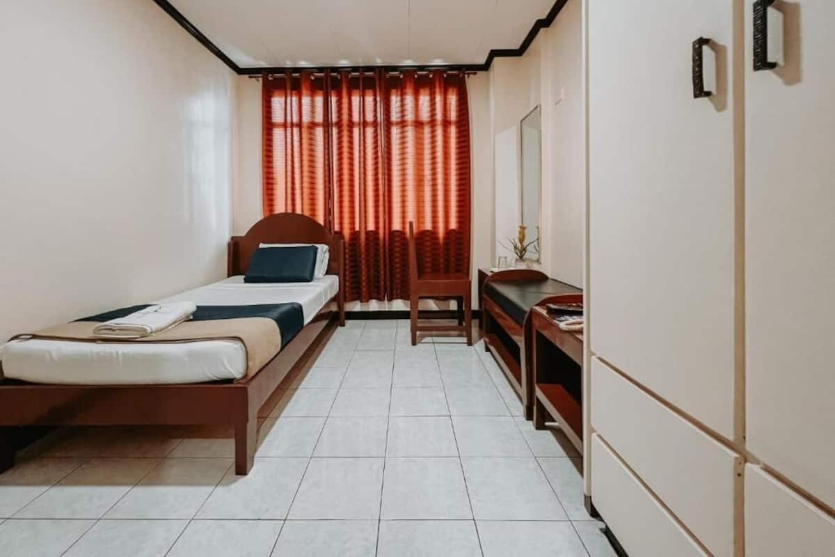 Une chambre à coucher avec un lit, un bureau, une chaise et une fenêtre avec des rideaux.