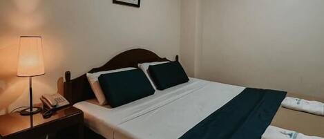 Una habitación de hotel con cama, mesita de noche con lámpara y un cuadro pequeño en la pared.