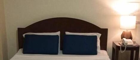 Habitación de hotel con una cama, dos almohadas, una lámpara de noche, un teléfono y un cuadro en la pared.