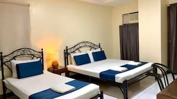 A room with two single beds, each with a blue and white bedspread, a bedside table with a lamp, and a chair.