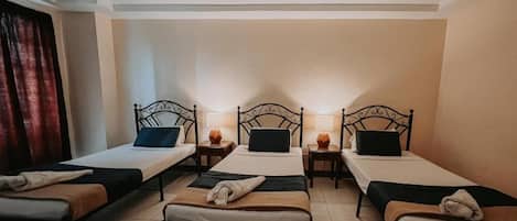 A hotel room with four single beds, each with a bedside table and lamp.