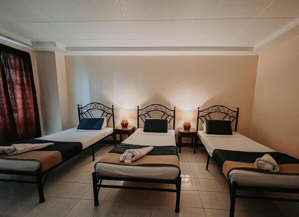 A hotel room with four single beds, each with a bedside table and lamp.