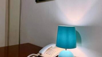 Una scrivania in legno con un telefono bianco e una lampada da tavolo verde acqua. Un quadro con un cerchio rosso e forme astratte è appeso al muro.