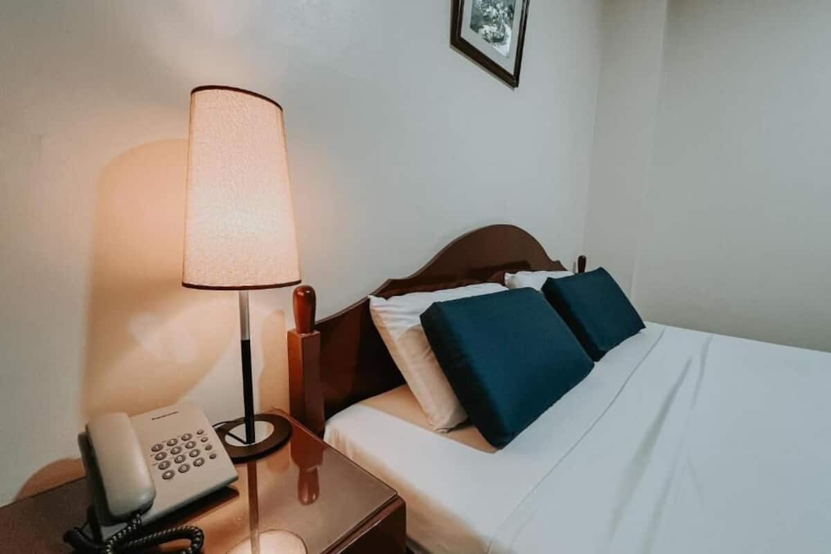 Une chambre d’hôtel avec un lit, une lampe de chevet et un téléphone sur une table de chevet.