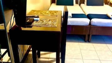 A hotel room with a desk, a computer, a bed, and a small table with a tray of food.