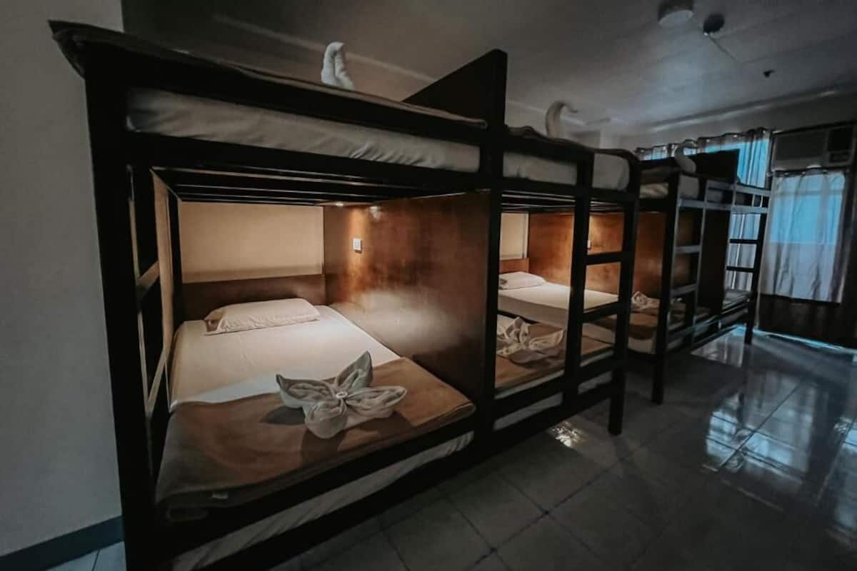Une chambre avec un lit superposé en bois, une petite fenêtre et une table de chevet avec une lampe.