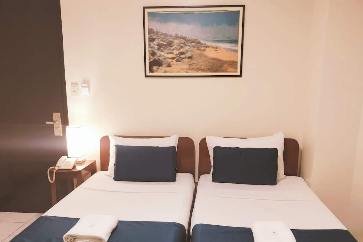 Une chambre d’hôtel avec deux lits, un tableau représentant une plage, un téléphone et une table de chevet.