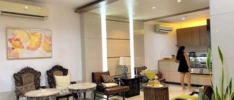 A spacious living area with a sofa, chairs, a coffee table, and a kitchen in the background.