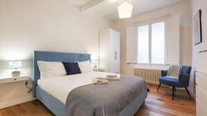 A bedroom with a bed, a chair, a wardrobe, and a window.