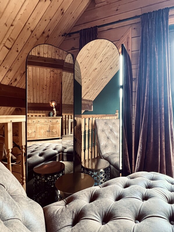 A cozy room with a high ceiling, wooden beams, a tufted sofa, a mirrored wall, and a small round table.