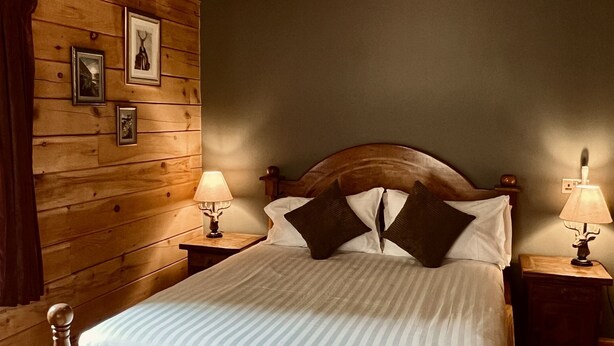 A wooden-framed bed with white bedding, two bedside lamps, and framed pictures on the wall.