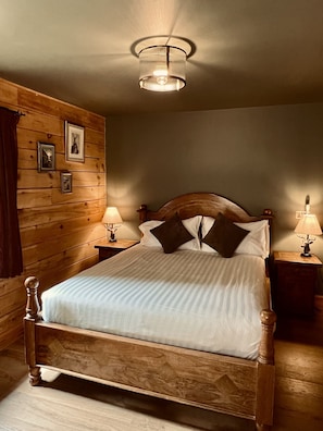 Una cama con estructura de madera, ropa de cama blanca, dos lámparas de noche y cuadros en la pared.