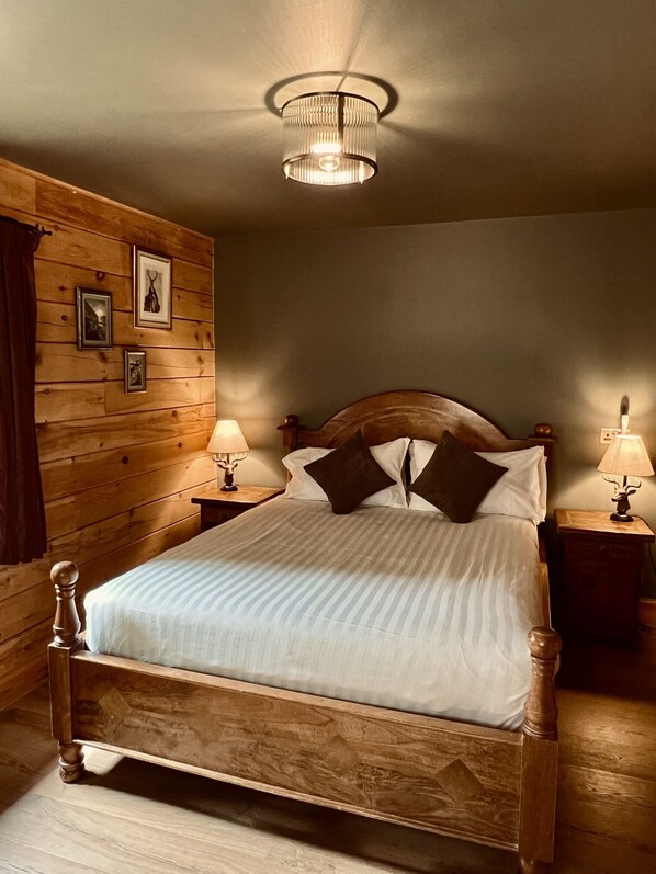Una cama con estructura de madera, ropa de cama blanca, dos lámparas de noche y cuadros en la pared.