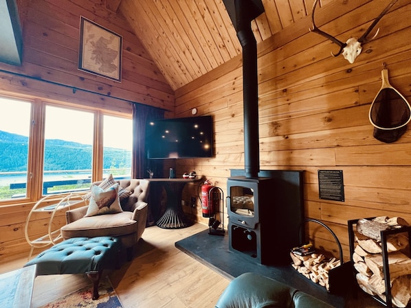 Interior acogedor de una cabaña con chimenea, asientos cómodos, un televisor y una vista panorámica.