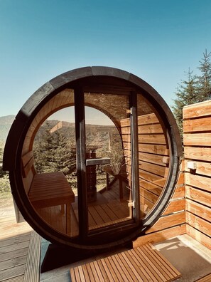 A wooden cabin with a circular window, wooden deck, and a view of a mountainous landscape.