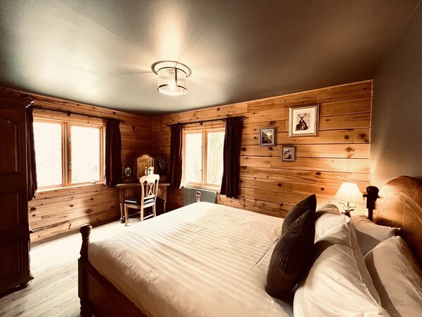 A wooden-paneled bedroom with a bed, a desk, and a chair.