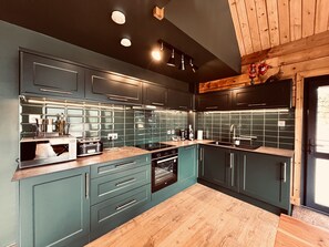 A modern kitchen with dark teal cabinets, a wooden countertop, and a built-in oven.