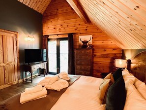 Een knus houten blokhut slaapkamer met een groot bed, een dressoir, een televisie en een deur naar een balkon.