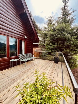 Una terraza de madera con un banco y una mesa, con vista a un área boscosa.
