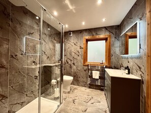 A modern bathroom with a glass-enclosed shower, a wooden-framed window, and a marble-tiled floor.