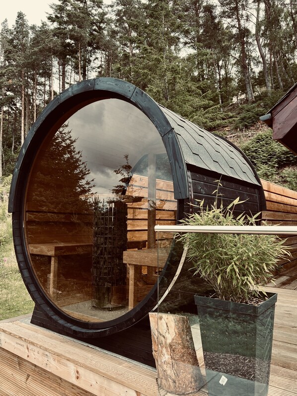 A cylindrical structure with a reflective surface, surrounded by wooden elements and greenery.
