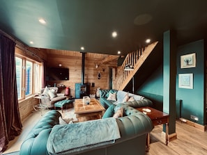 A cozy living room with a sectional sofa, a wooden floor, a fireplace, and a staircase.