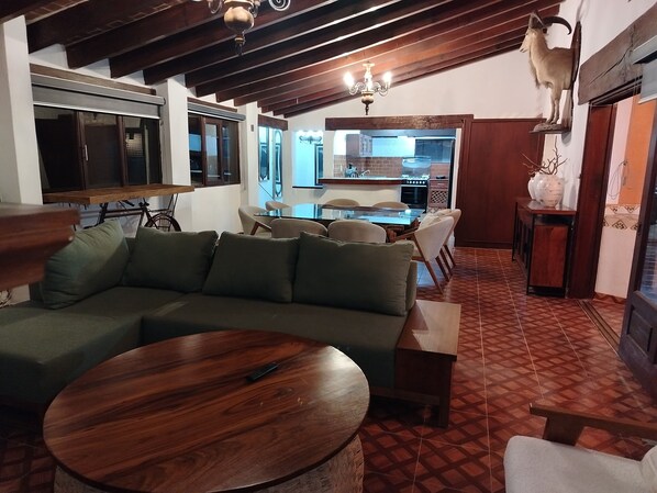A cozy living room with a green sofa, a wooden coffee table, and a dining area with a glass table and chairs.