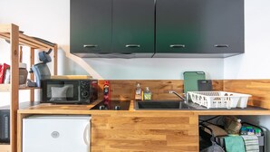 Une cuisine compacte équipée d’un four à micro-ondes, d’un grille-pain et d’un évier. Des placards sont situés en hauteur et un petit réfrigérateur en dessous.