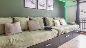Un espace de vie aux couleurs vertes, comprenant un canapé, des coussins et offrant une vue sur l’extérieur.