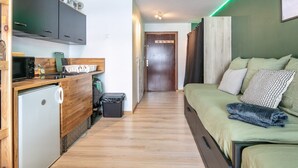 Un espace de vie compact comprenant un coin cuisine, un lit avec une literie verte et un meuble en bois.