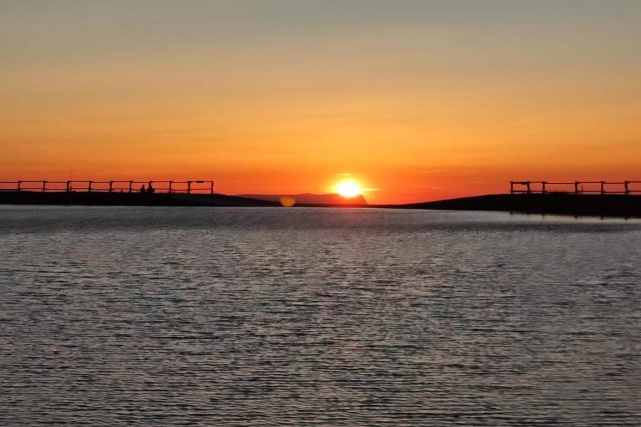 A sunset over a calm body of water with a bridge in the foreground.