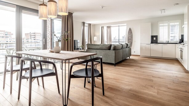Eine moderne Wohnung mit Essbereich, einer Couch, einer Küche und großen Fenstern mit Blick auf die Stadt.