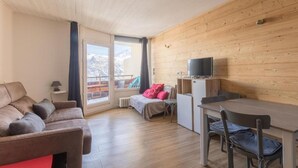 Ein gemütliches Zimmer mit Holzbalkendecke, einer Couch, einem Bett, einem Fernseher und einem Essbereich.