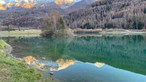 Ein ruhiger See mit Bergelandschaft im Hintergrund, umgeben von bewaldeten Hügeln.