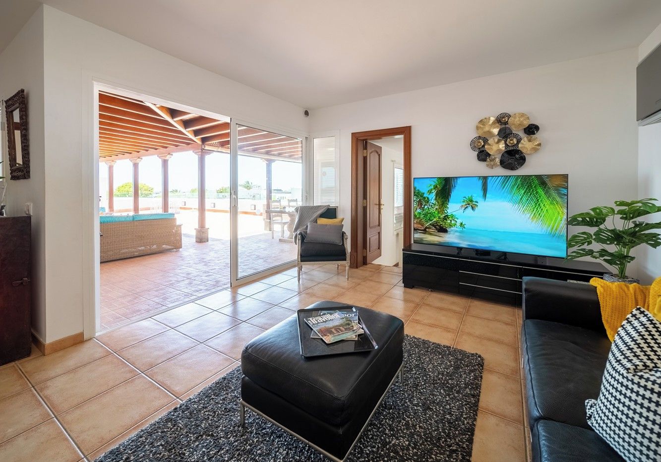 A living room with a sofa, ottoman, and a flat-screen TV. There is a sliding glass door leading to an outdoor area with a covered patio.