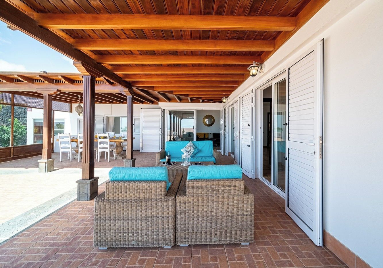 Une terrasse extérieure couverte, aménagée avec des meubles en osier, comprenant un coin repas et offrant une vue sur la maison.