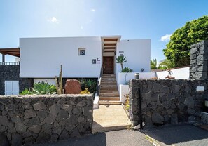 A modern building with a white facade, a wooden staircase leading to the entrance, and a stone wall in the foreground.