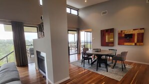 A spacious living area with a fireplace, a dining table with chairs, and a balcony with a view of the outdoors.