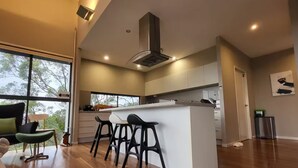 A modern kitchen with a central island, bar stools, and a view of the outdoors through large windows.