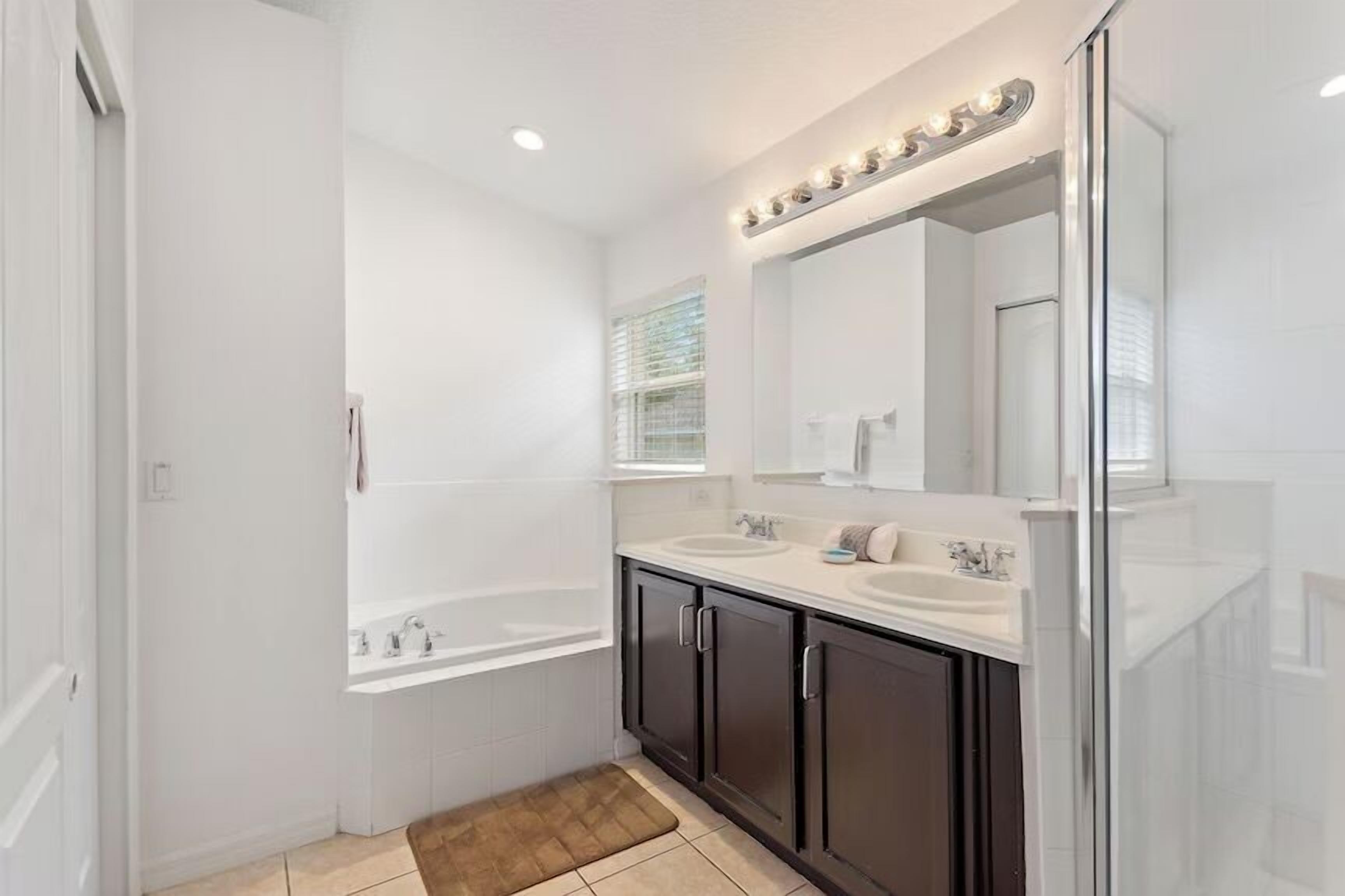 A modern bathroom with a large mirror, two sinks, a bathtub, and a shower.